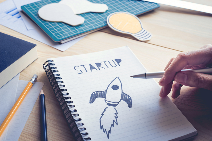 Businessman Holding Pen With Drawing Startup Text On Notebook.