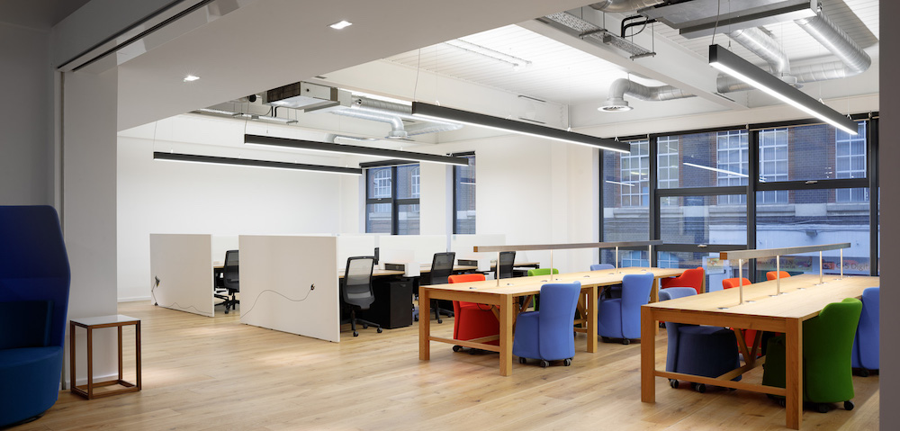Us&Co's coworking space featuring office desks available to rent in East London, Stratford. Vibrant coloured chairs & floor to ceiling windows decorate the space.