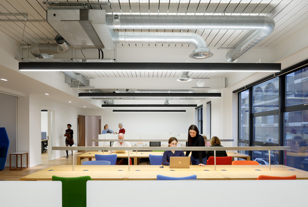 Us&Co Stratford, East London hot desk for rent in a co-working space with blue & orange office chairs and long wooden tables.