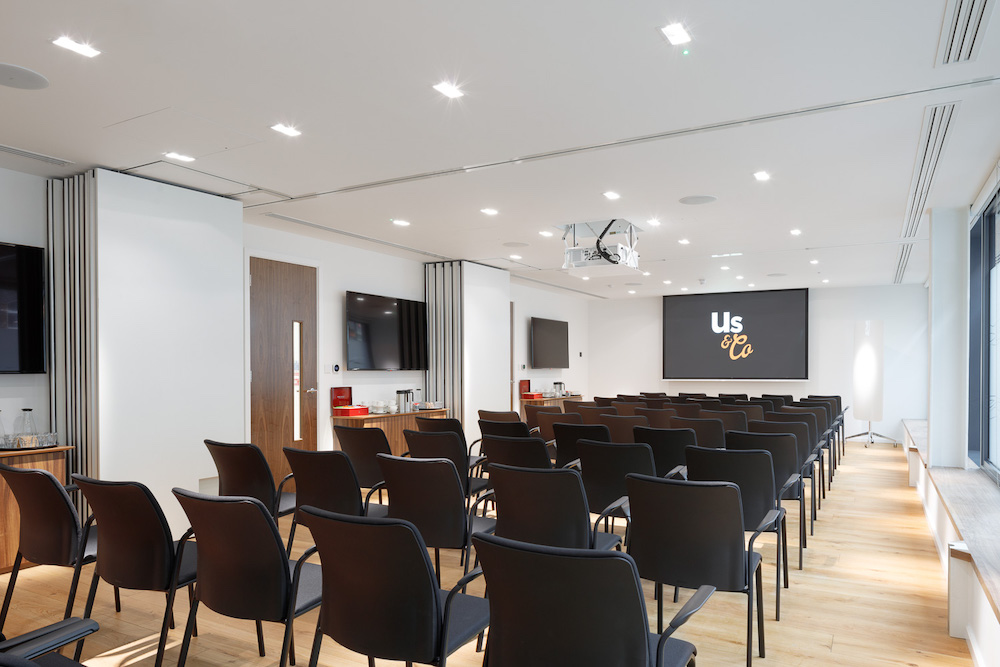 Us&Co meeting room in Stratford, East London. Professional conference venue with black chairs lined up and huge HD screen.